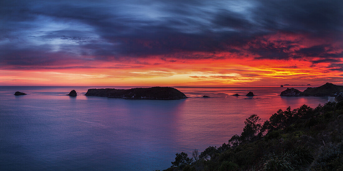 Ein feuriger Dämmerungshimmel bricht über die Inseln vor der Coromandel-Halbinsel, Waikato, Nordinsel, Neuseeland, Pazifik