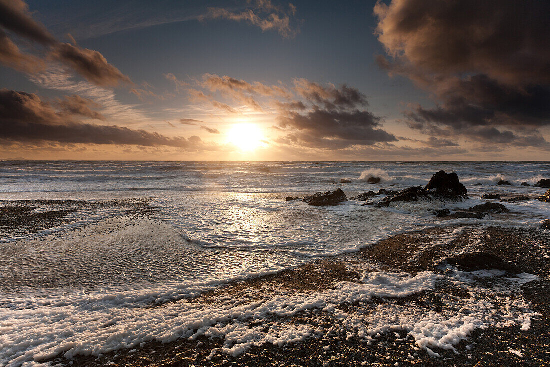 Storm surf and hills of sea foam under a sunset skyscape at Tyn Tywyn beach, Rhosneigr, West Anglesey, Wales, United Kingdom, Europe
