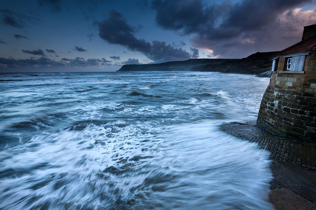 Nordsee-Wellen, die über gepflasterte Slipway bei Sonnenuntergang in Robin Hoods Bay, North Yorkshire, Yorkshire, England, Großbritannien, Europa zusammenstoßen
