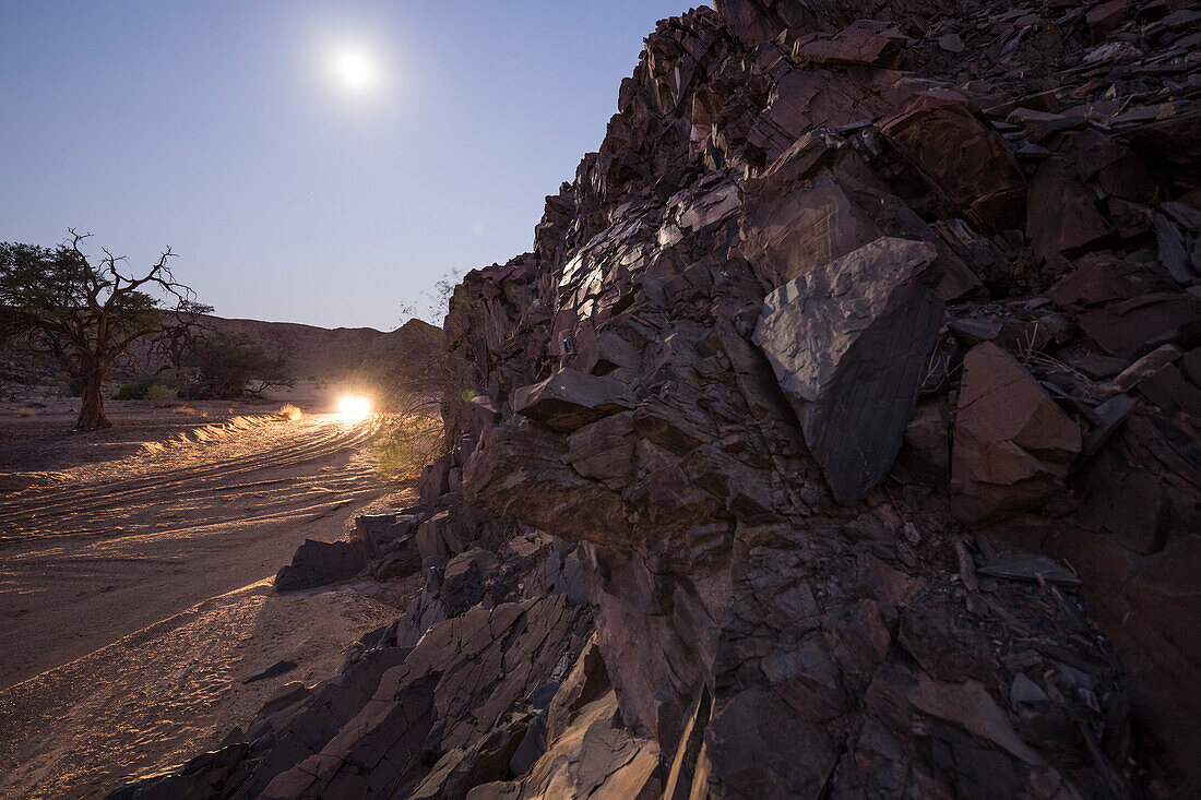 Ein Geländewagen fährt bei Vollmond durch das trockenes Doros-Flussbett, Damaraland, Kunene, Namibia