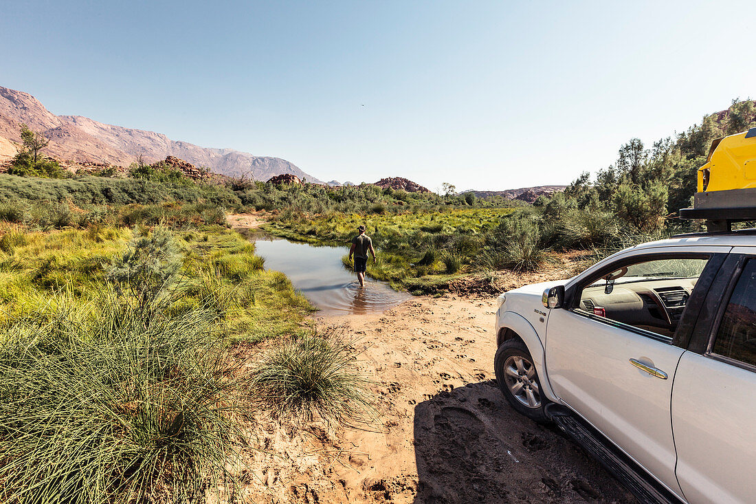 Before crossing the Ugab river from Kunenen to Erongo, the driver checks the water depth. In the Background the Brandberg mountain, Erongo, Damaraland, Namibia, Africa