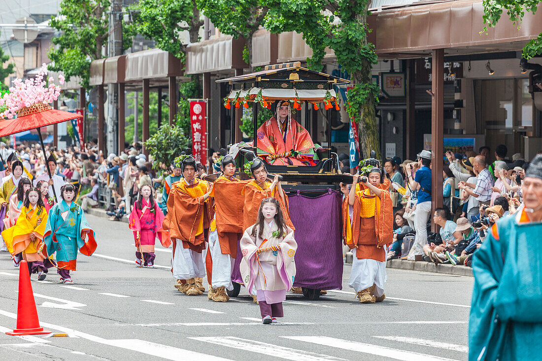 Hochgestellte Frau in Trage die von jungen Männern gezogen und Mädchen in Kimono begleitet wird beim Festumzug Aoi Matsuri in Kyoto, Japan