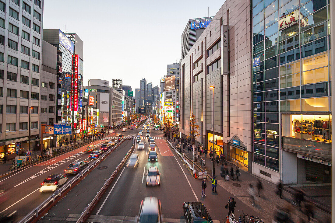 Koshu Kaido Straße mit Park Hyatt, Plakaten und bewegten Autos zur blauen Stunde, Shinjuku, Tokio, Japan