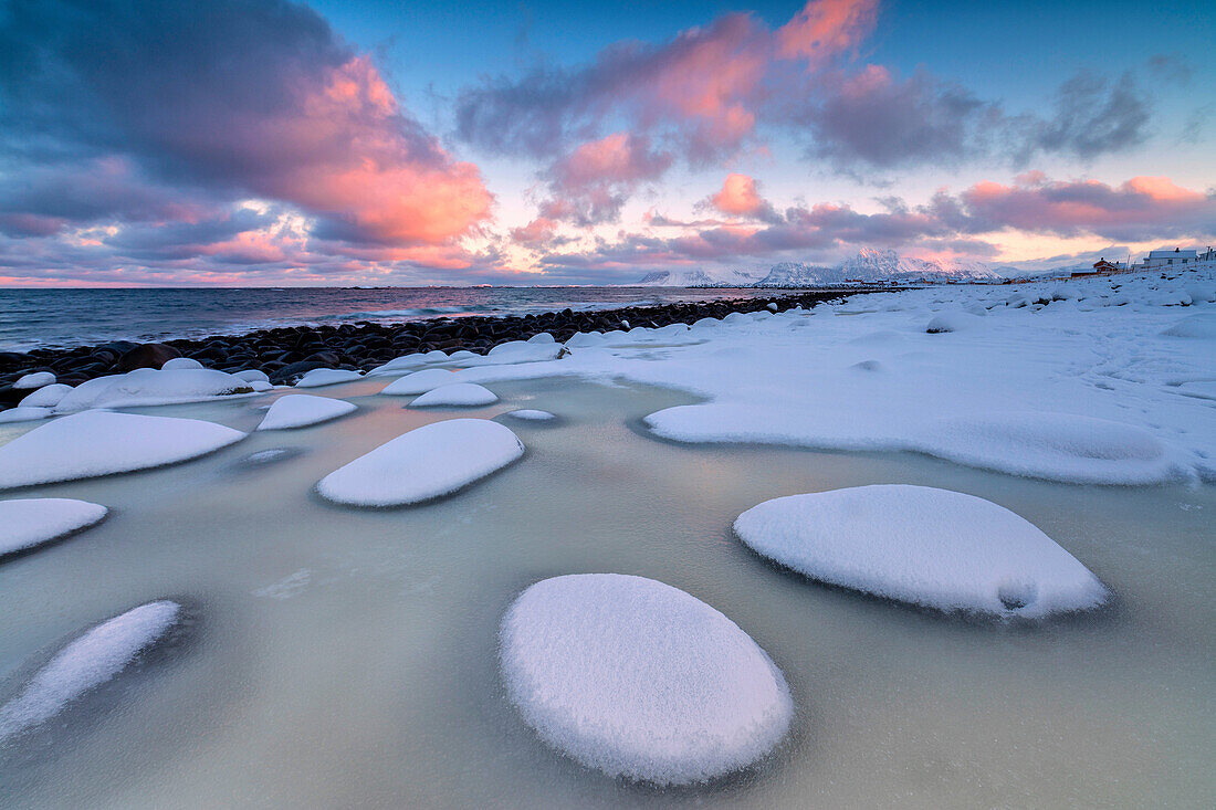 Dawn on the cold sea surrounded by snowy rocks shaped by wind and ice at Eggum Vestvagøy Island Lofoten Islands Norway Europe.