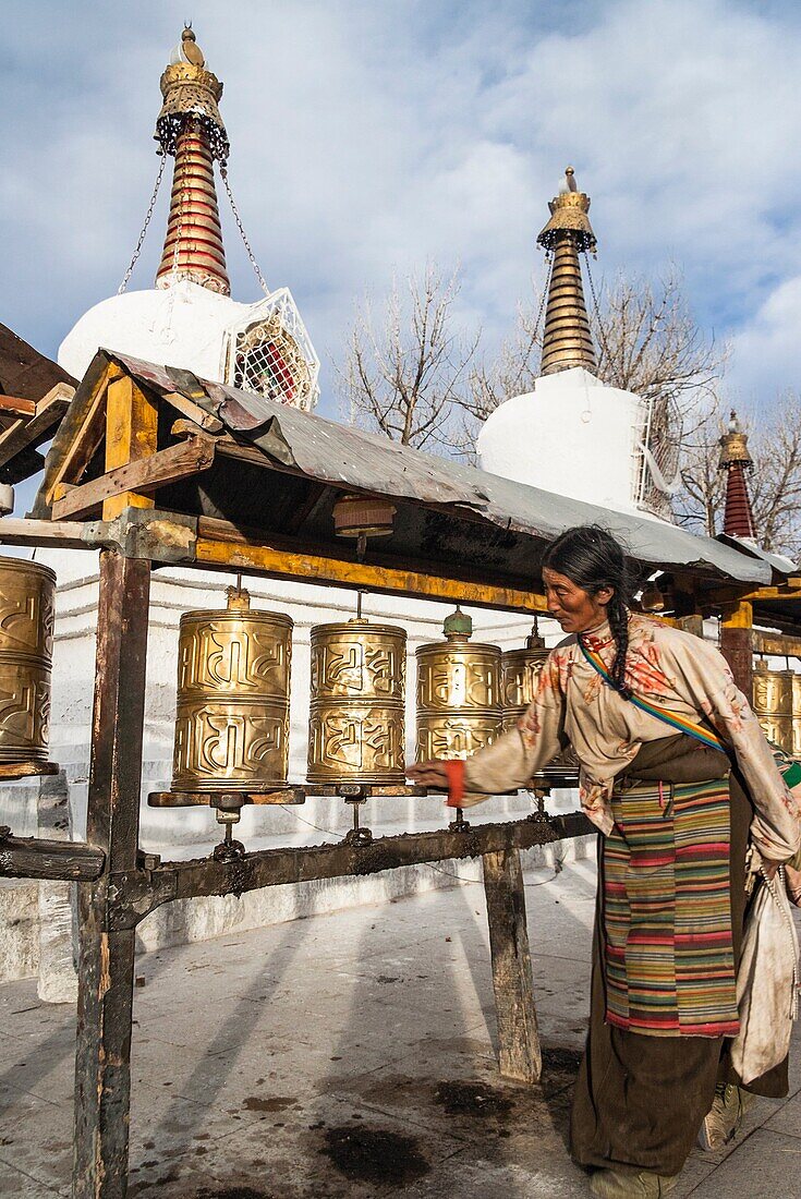 Tibetan pilgrim by prayer wheels and stupas in Lhasa, Tibet.