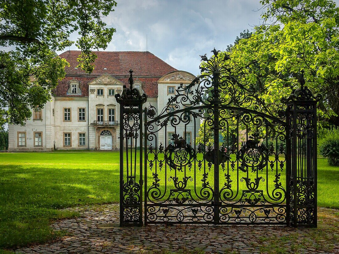An old solitary wrought-iron locked gate in front of an abandoned baroque manor house in Mecklenburg-Pomerania, Germany, standing in a park environment.