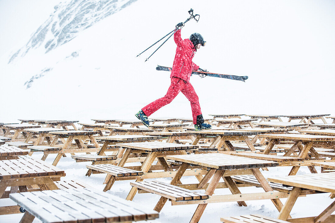 Junger Skifahrer läuft über Tische eines Restaurants in den Bergen, Kaprun, Salzburg, Österreich