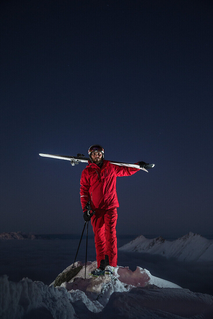 Junger Skifahrer steht auf dem Gipfel eines Berges über den Wolken bei Nacht, Kaprun, Salzburg, Österreich