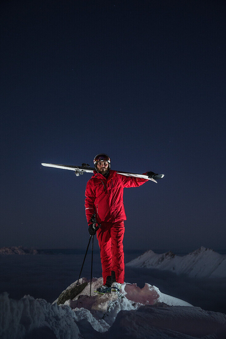 Young male skier standing on the top of a mountain over the clouds at night, Kaprun, Salzburg, Austria