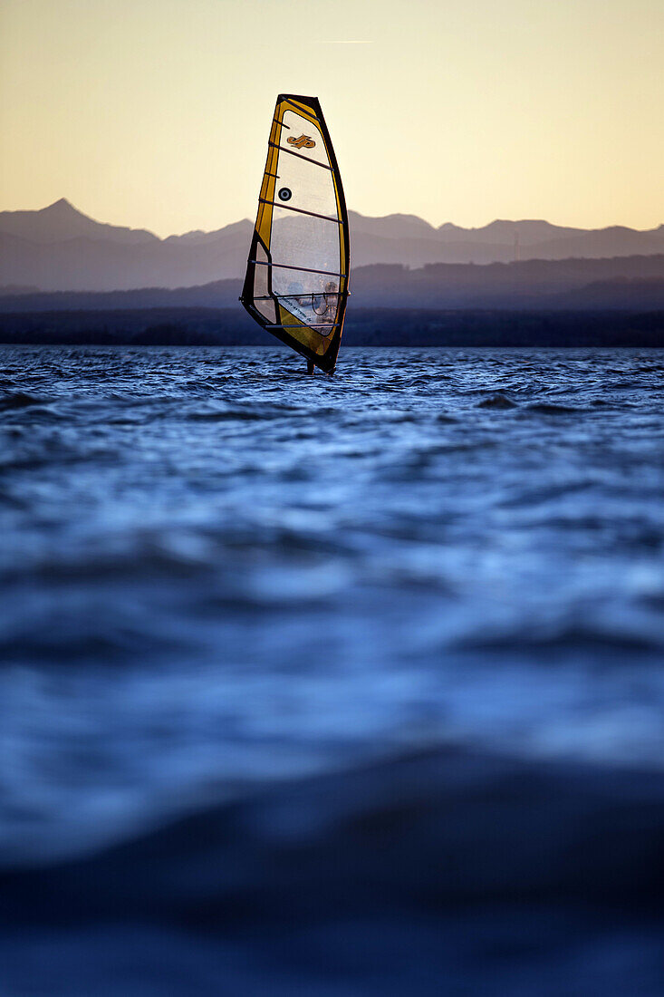 Junger Mann windsurft bei Sonnenuntergang, Ammersee, Bayern, Deutschland