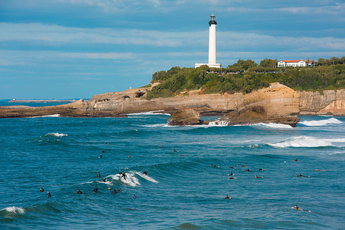 Surfers ride waves with lighthouse behind