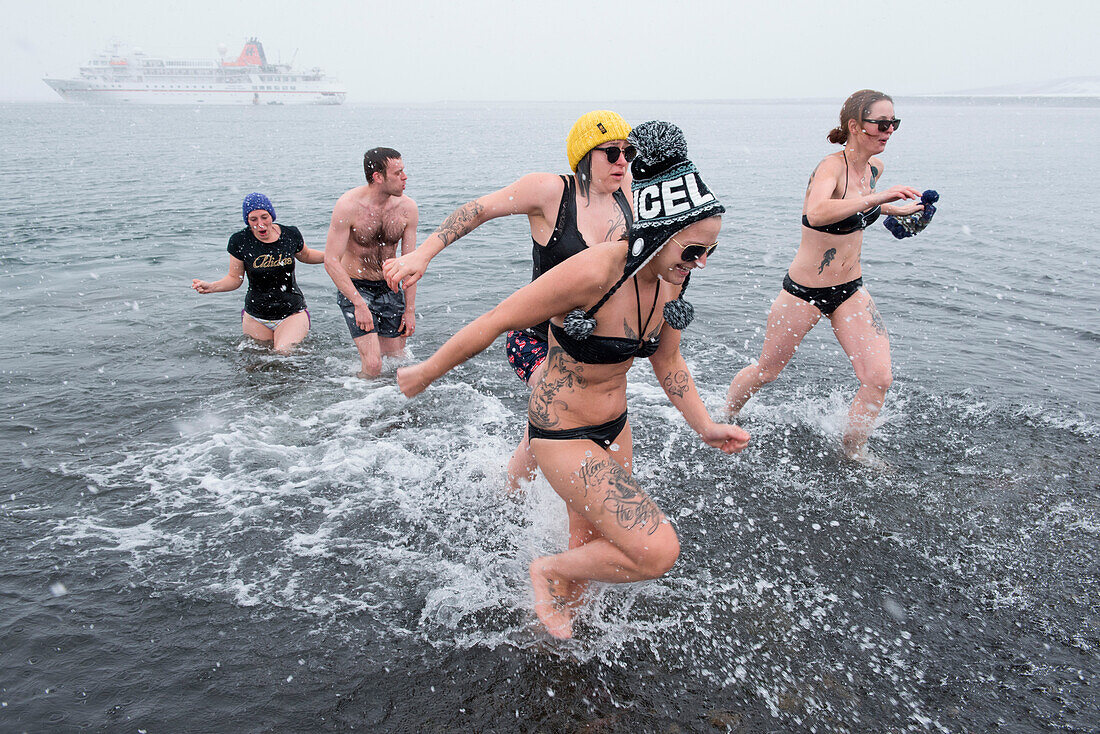 People run and splash in Antarctic waters with expedition cruise ship MS Bremen (Hapag-Lloyd Cruises) behind