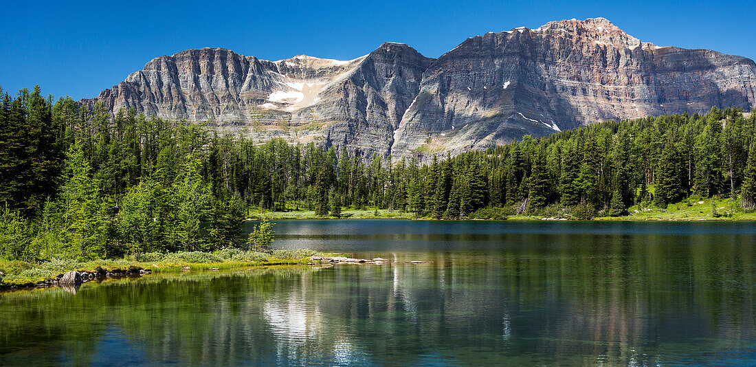 'Panorama of mountain range reflecting off an alpine lake with blue sky; Banff, Alberta, Canada'