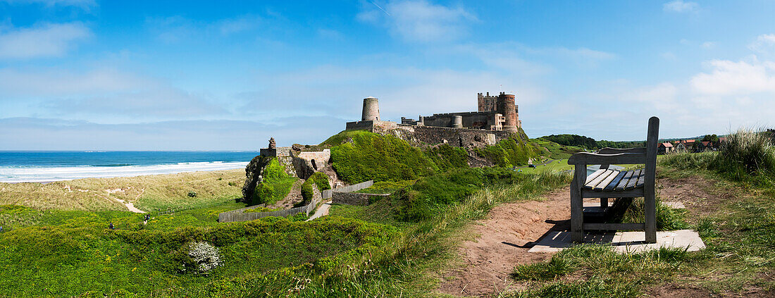 'A bench with a view of the ocean and Bamburgh Castle in the distance; Bamburgh, Northumberland, England'