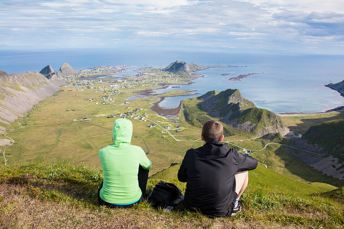 Couple on top of peak admire sea framing the village of Sorland, Vaeroy Island, Nordland county, Lofoten archipelago, Norway, Scandinavia, Europe
