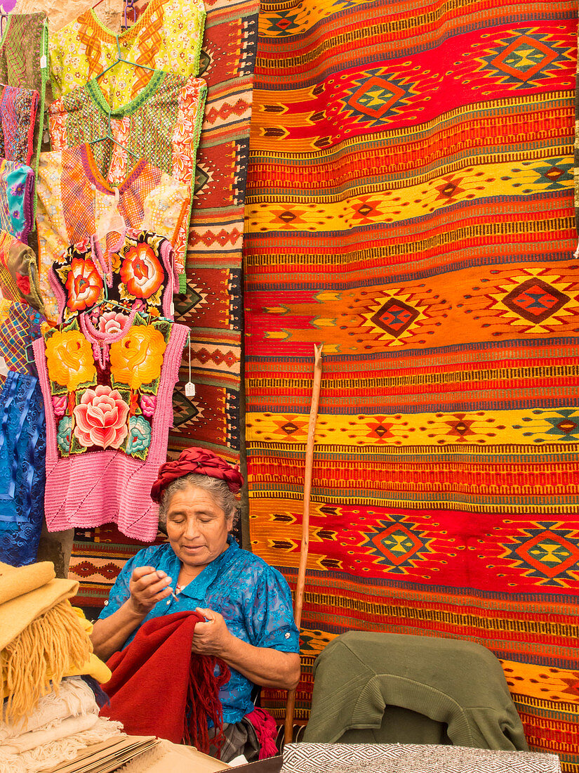 Woman sewing in market with background of handmade rugs, Oaxaca, Mexico, North America
