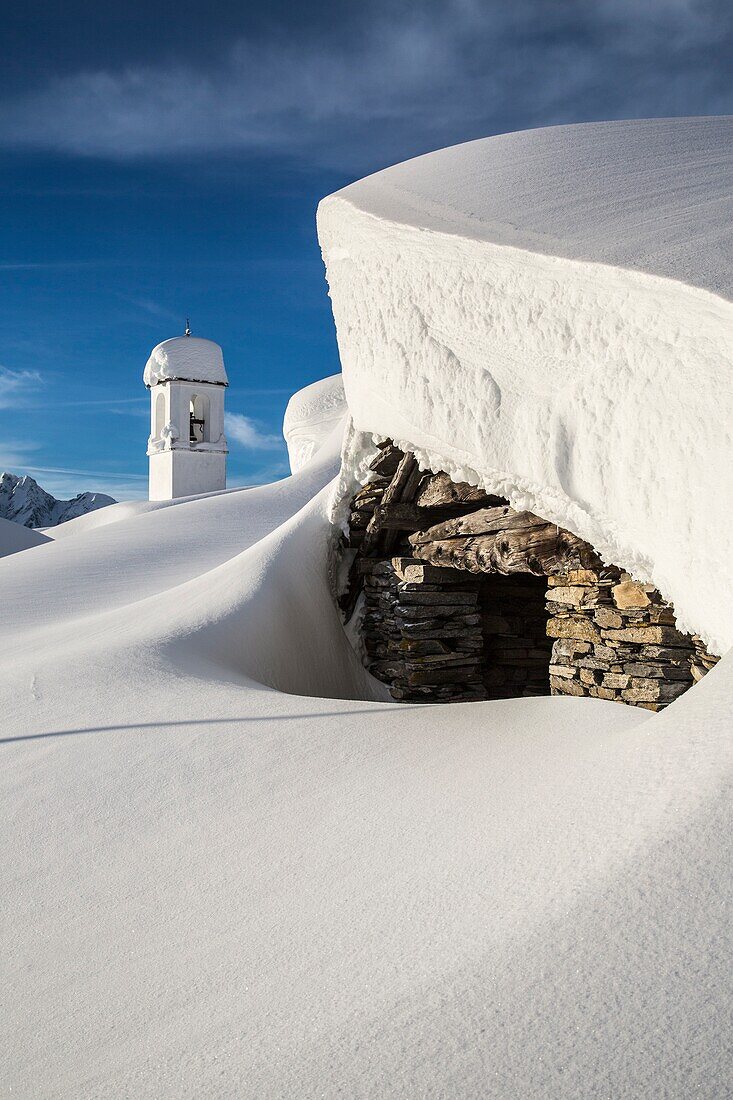 Mountain hut covered in snow with the bell tower of the Alpe Scima in the background, Valchiavenna, Valtellina Lombardy Italy Europe
