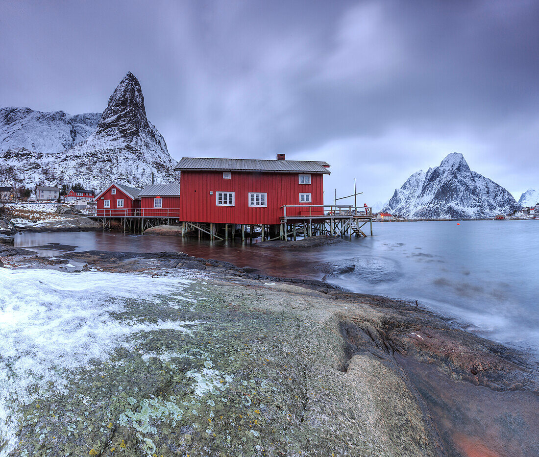 Typical red houses in Reine landscape with its cold sea and snow capped peaks, Lofoten Islands Norway Europe