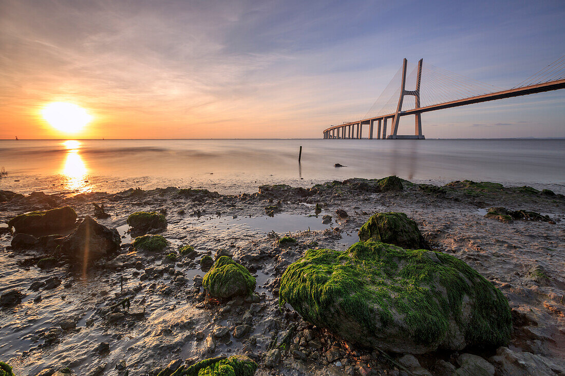 The sun rises on the Vasco da Gama Bridge that spans the Tagus River in Parque das Na+º+Áes Lisbon Portugal Europe