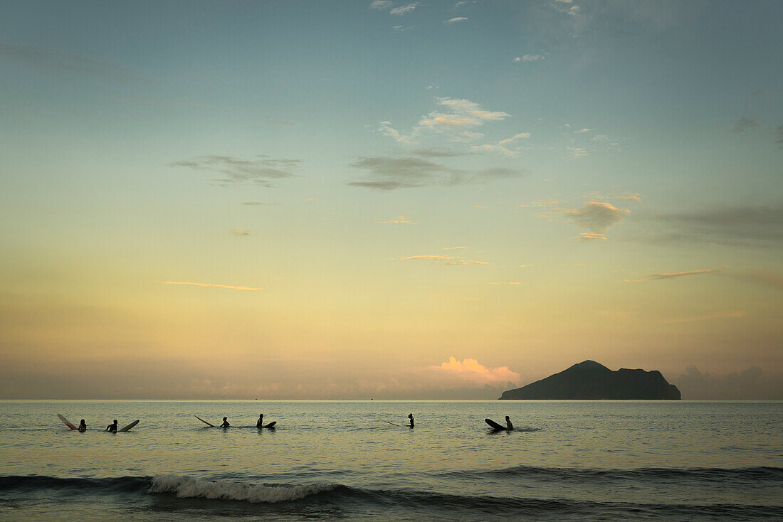 'Surfers waiting for waves and Turtle island behind them at sunset, Waiao beach, Yilan County; Taiwan, China'