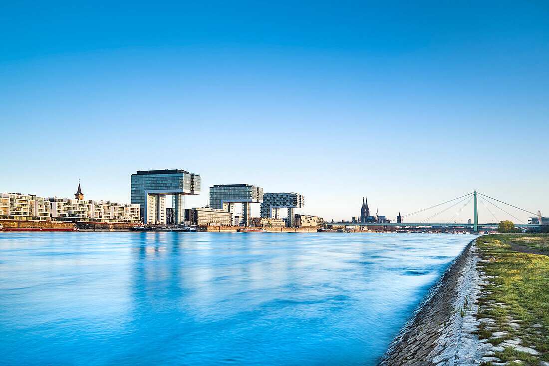 View over river Rhein towards Rheinau harbour with crane houses, Cologne Cathedral, Cologne, North Rhine-Westphalia, Germany