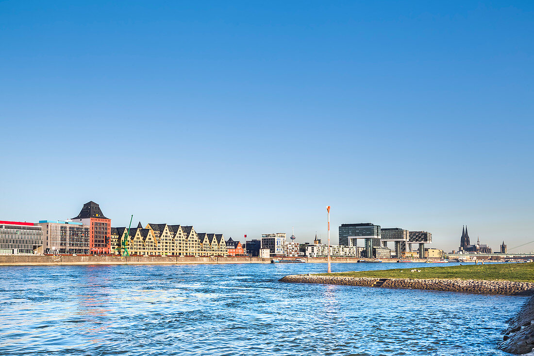 View over river Rhein towards Rheinau harbour with crane houses, Cologne Cathedral, Cologne, North Rhine-Westphalia, Germany