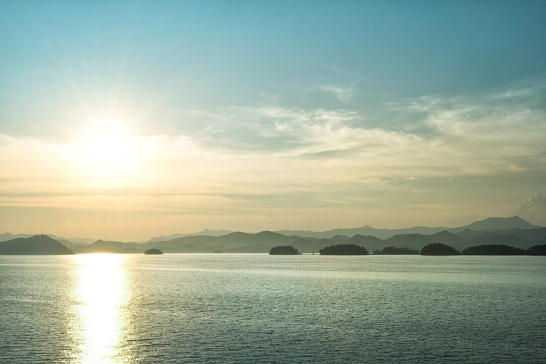 The sun about to set over the mountains surrounding Qiandao (Thousand Islands) Lake, Chunan, Zhejiang, China, Asia