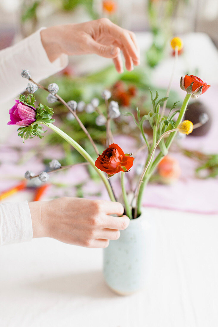 Beschnittenes Bild einer Frau, die Blumen in einer Vase auf dem Tisch arrangiert