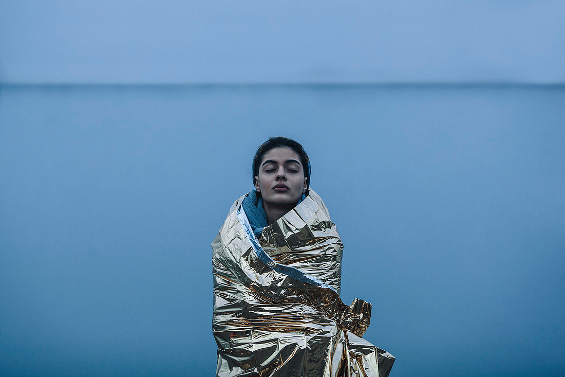 Teenage girl with eyes closed wrapped in golden plastic against lake