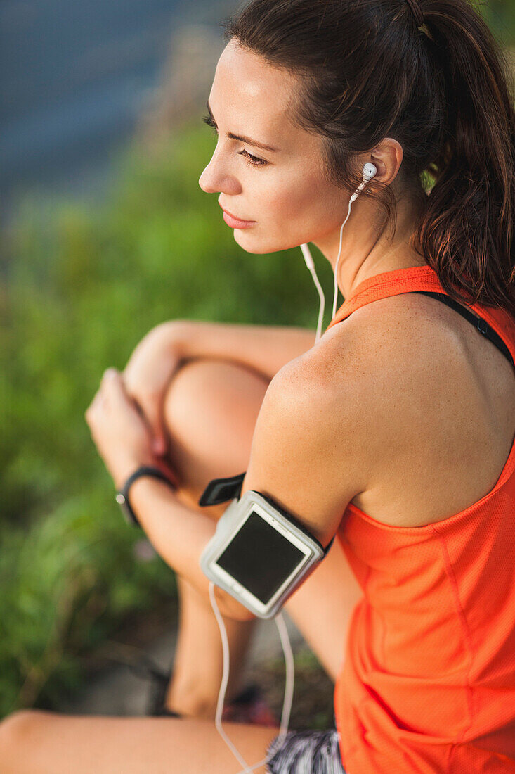 High angle view of woman sitting by pond while listening to music at park