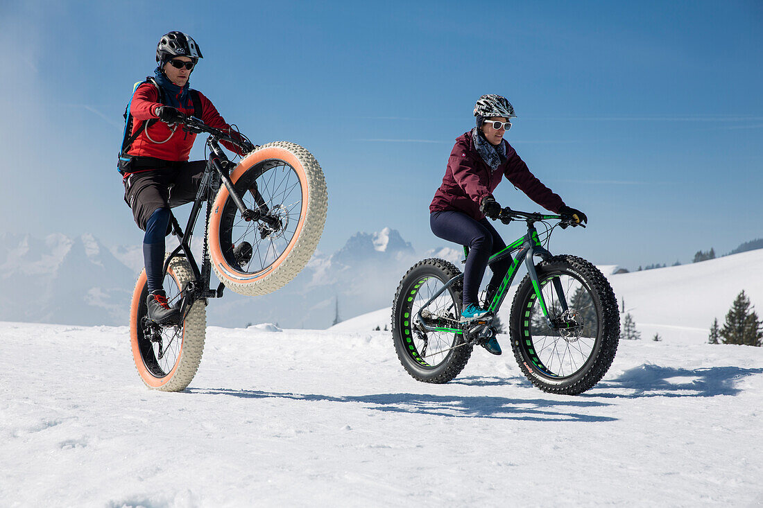 A young man (performing a wheelie) and young woman on fatbikes, snowbike, mountainbike at Sparenmoos above Gstaad, Bernese Oberland, Switzerland