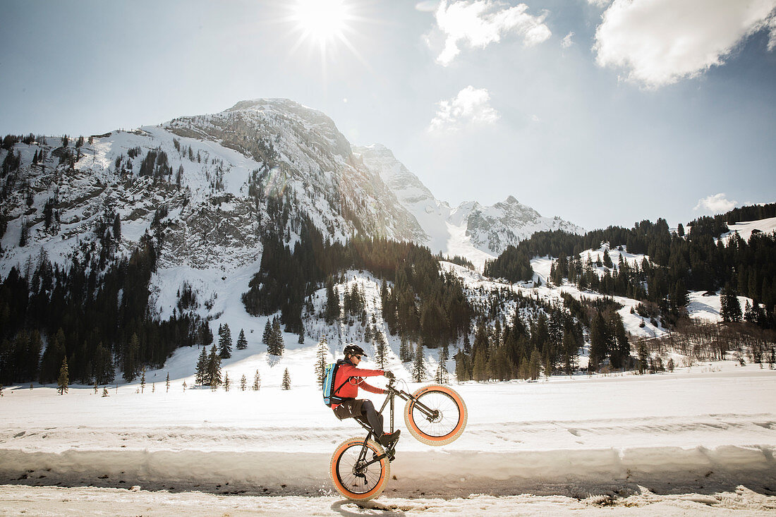 A young man performs a wheelie on a fatbike, snowbike, mountainbike  at Lauenensee near Gstaad, Bernese Oberland, Switzerland