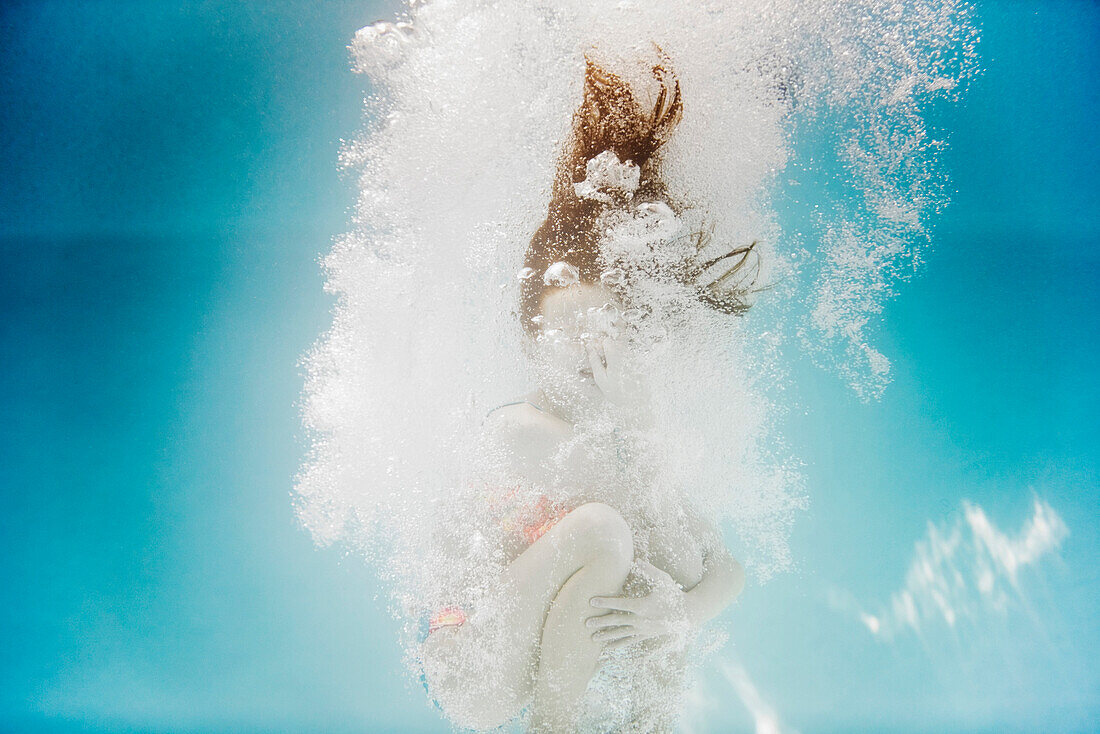 Caucasian girl swimming underwater holding nose