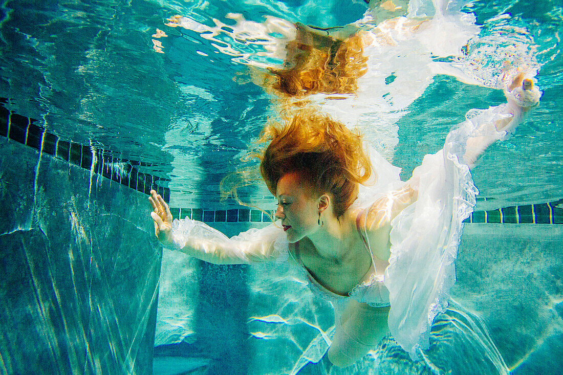 Caucasian woman wearing dress swimming underwater