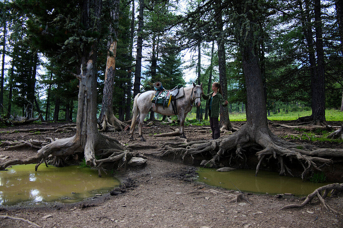 Caucasian girl petting horse in forest near puddles