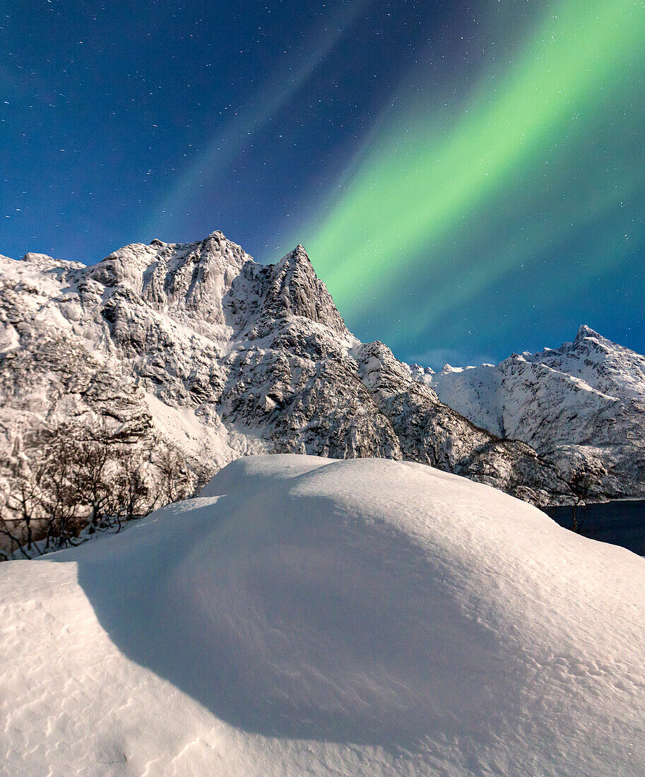 Northern Lights illuminate the snowy peaks and the blue sky during a starry night Budalen Svolvaer Lofoten Islands Norway Europe