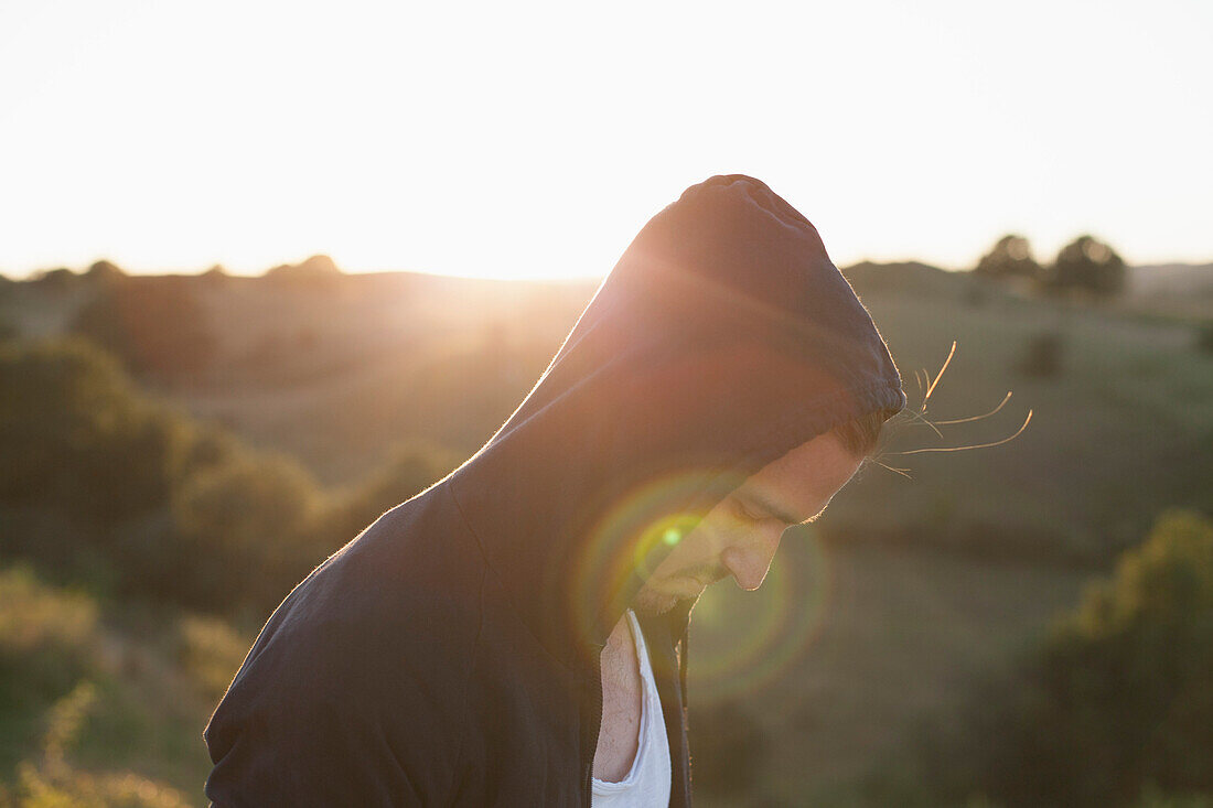 Side view of man wearing hooded jacket on field during sunny day