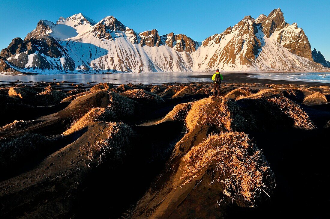 A man admires the Stokksnes mountains in the warm sunset light, Iceland
