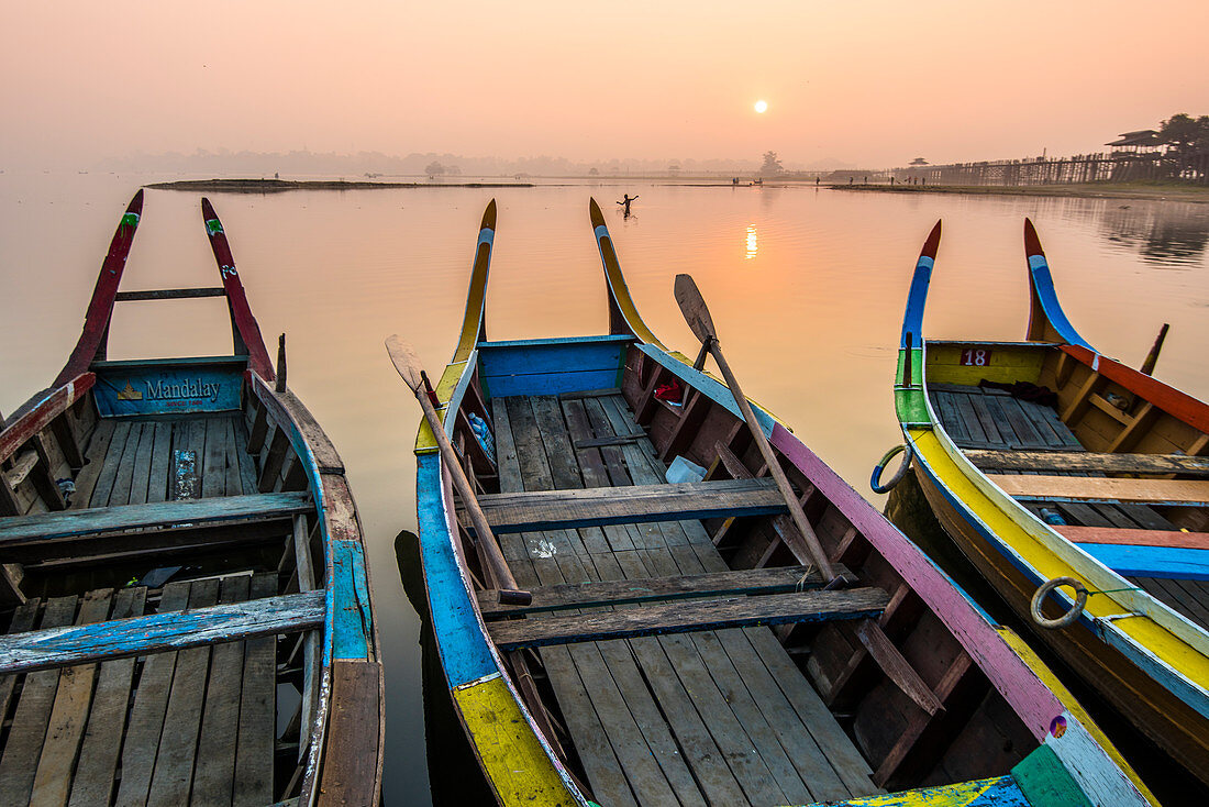 Amarapura, Mandalay region, Myanmar, Colorful boats moored on the banks of the Taungthaman lake at sunrise, with the U Bein bridge in the background