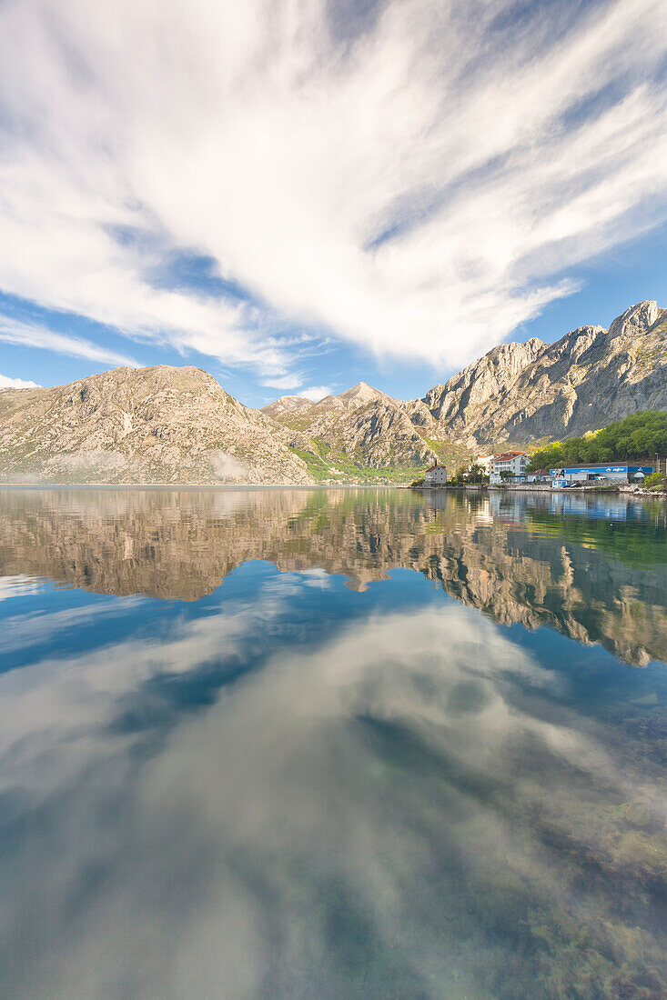 In the Kotor bay the sea is surrounded by mountains that are reflected in the calm water in the morning, in the corner of the picture the village of Ljuta, Montenegro