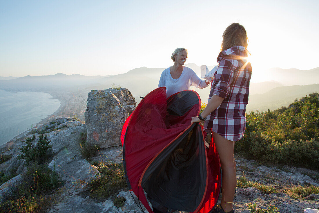 Mother and teenage daughter set up tent on hilltop above sea