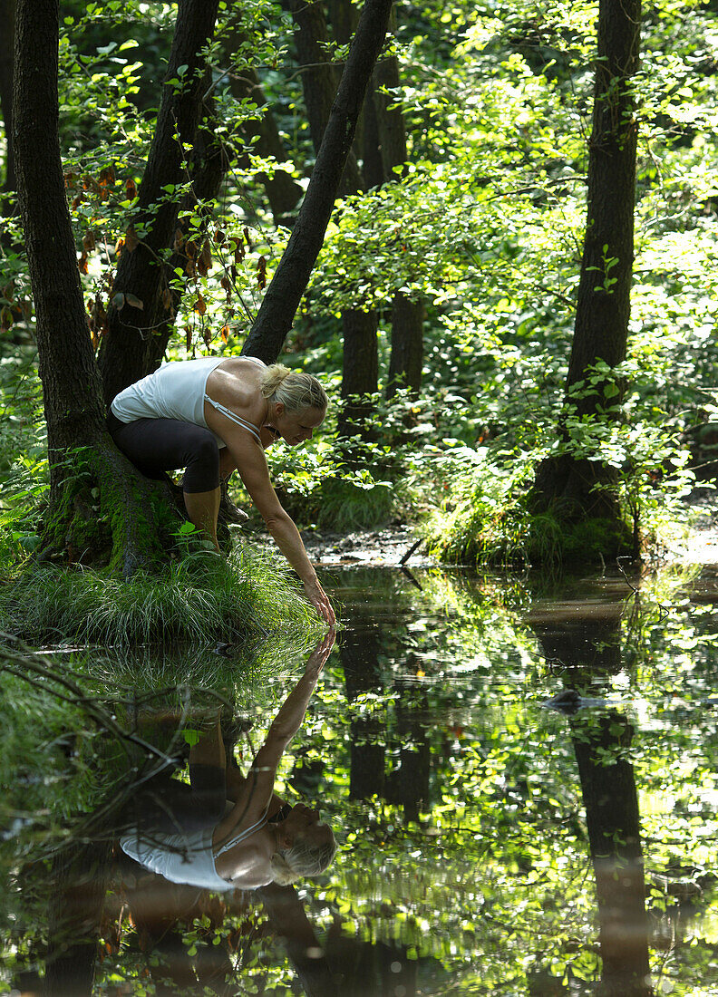 Woman touches surface of forest pond
