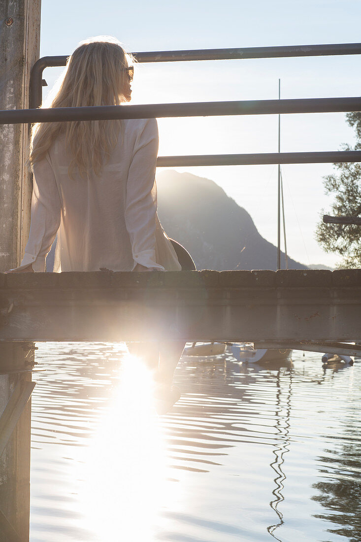 Woman relaxes on wooden pier, looks across lake