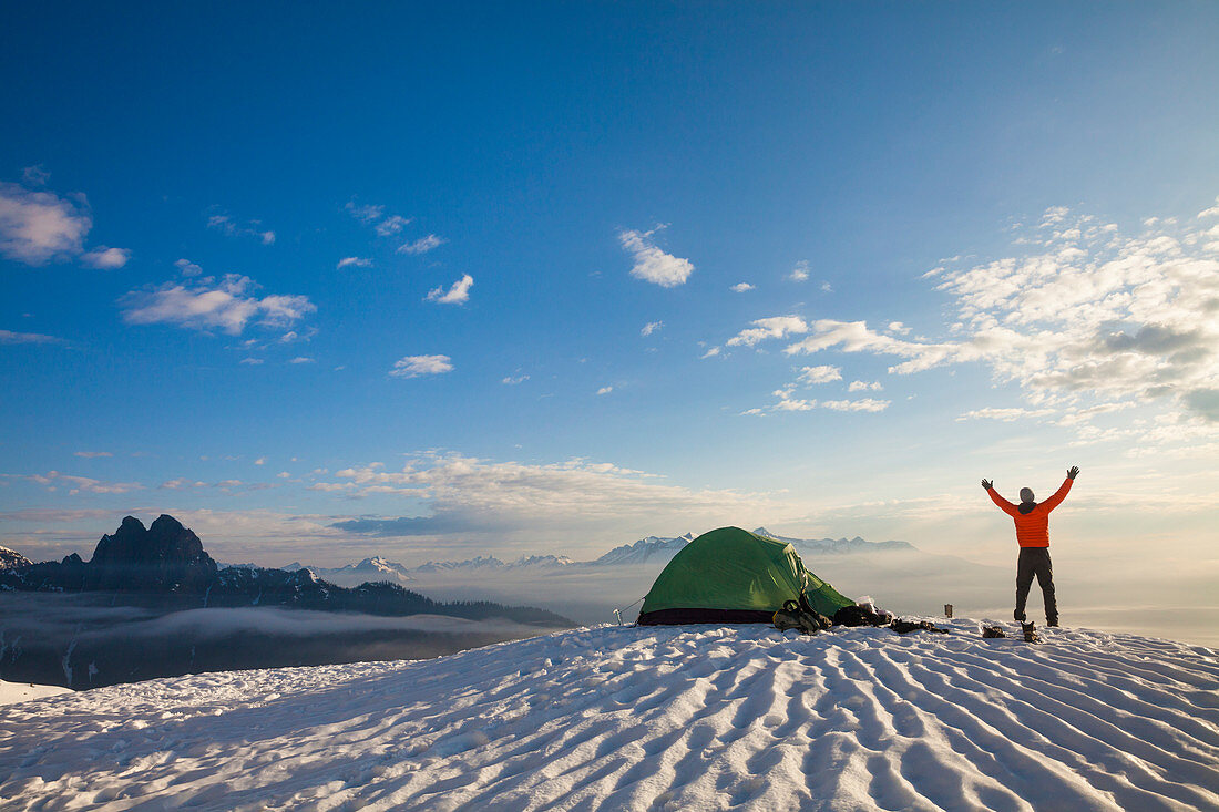 A Camper Lifting His Hand As He Watches The Sunrise From His Campsite On A Snow Covered Mountain