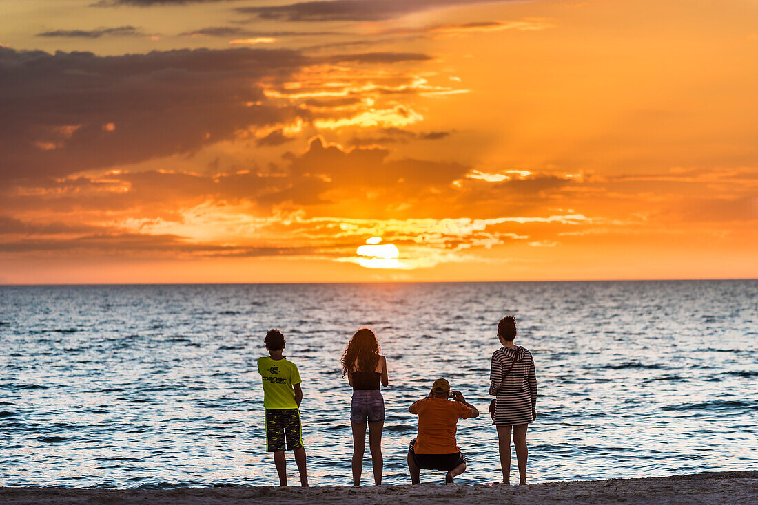 Eine Familie am Strand vom Golf von Mexiko fotografiert den Sonnenuntergang, Fort Myers Beach, Florida, USA