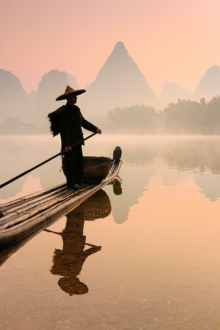 Chinese fisherman fishing with cormorant birds on a bamboo raft in Li Jang River, Yangshuo, Guilin, Guangxi region, China on December 25, 2006. Like their ancestors, this fisherman uses cormorants to fish at dusk and dawn, using lamps to help the birds ca
