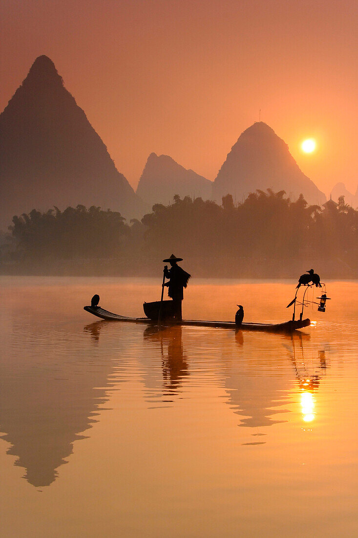 Chinese fisherman fishing with cormorant birds on a bamboo raft in Li Jang River, Yangshuo, Guilin, Guangxi region, China on December 25, 2006. Like their ancestors, this fisherman uses cormorants to fish at dusk and dawn, using lamps to help the birds ca