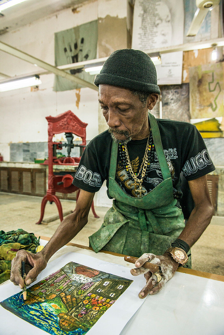 'A male Cuban artist painting a Cuban street scene, cigar in hand, in El Taller Experimental de Gr?ífica (Experimental Graphic Studio''), a cooperative graphic print shop and art studio in Old Havana or Habana Vieja, La Habana, Cuba.'''