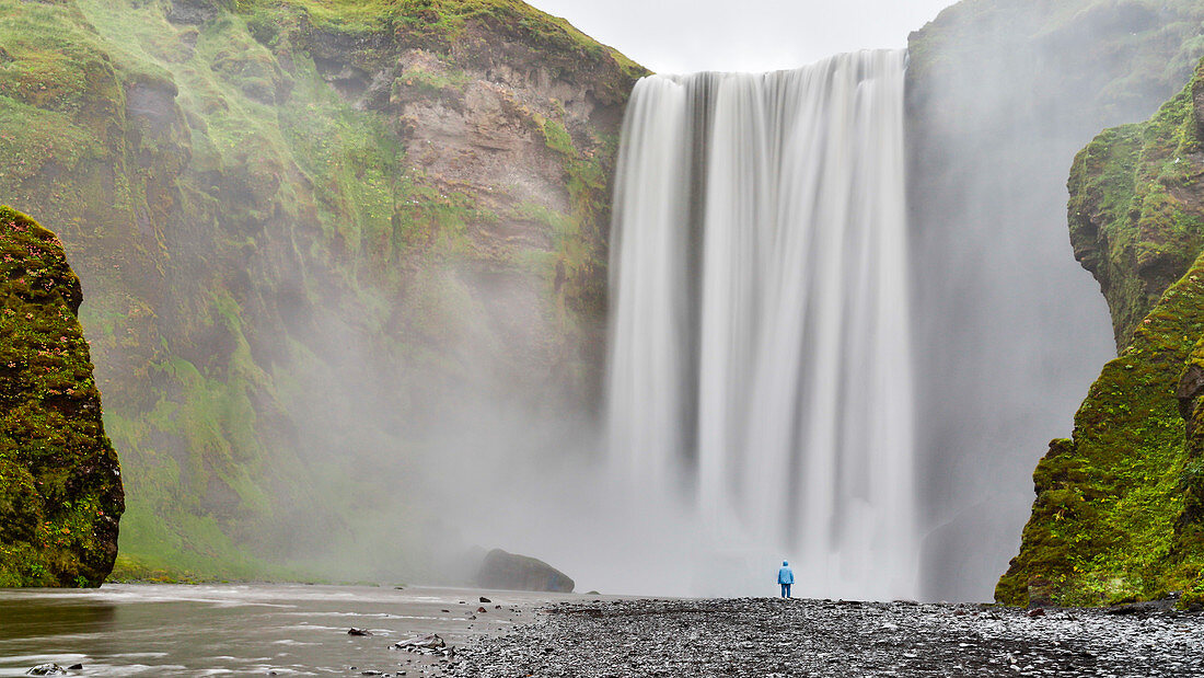 Person Standing In Front Of Skogafoss Waterfall In Iceland