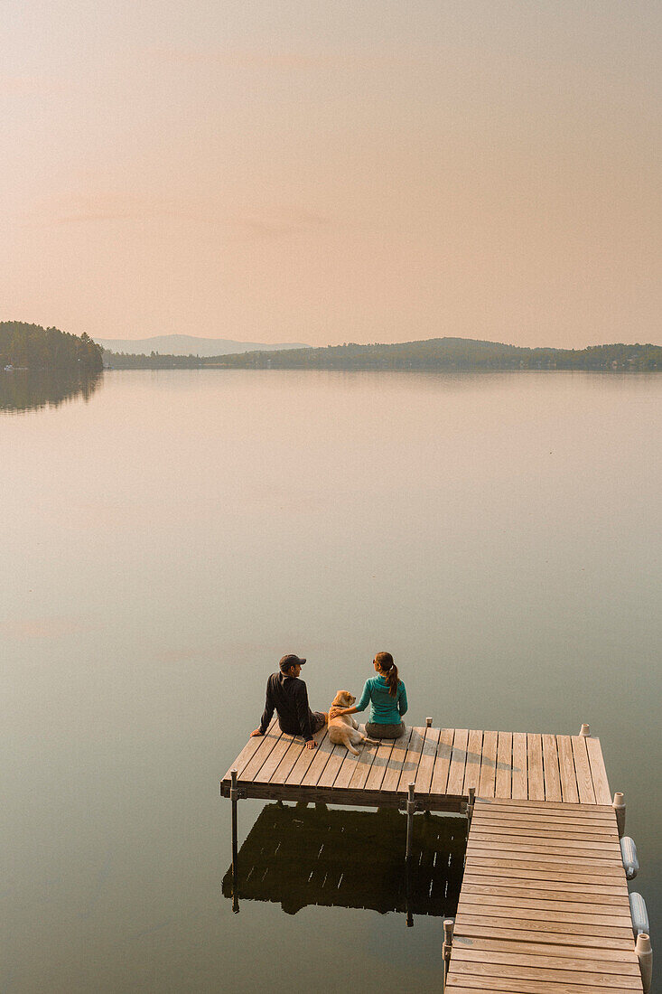 View Of Man And Woman With Dog Sitting On Edge Of Dock On Caspian Lake